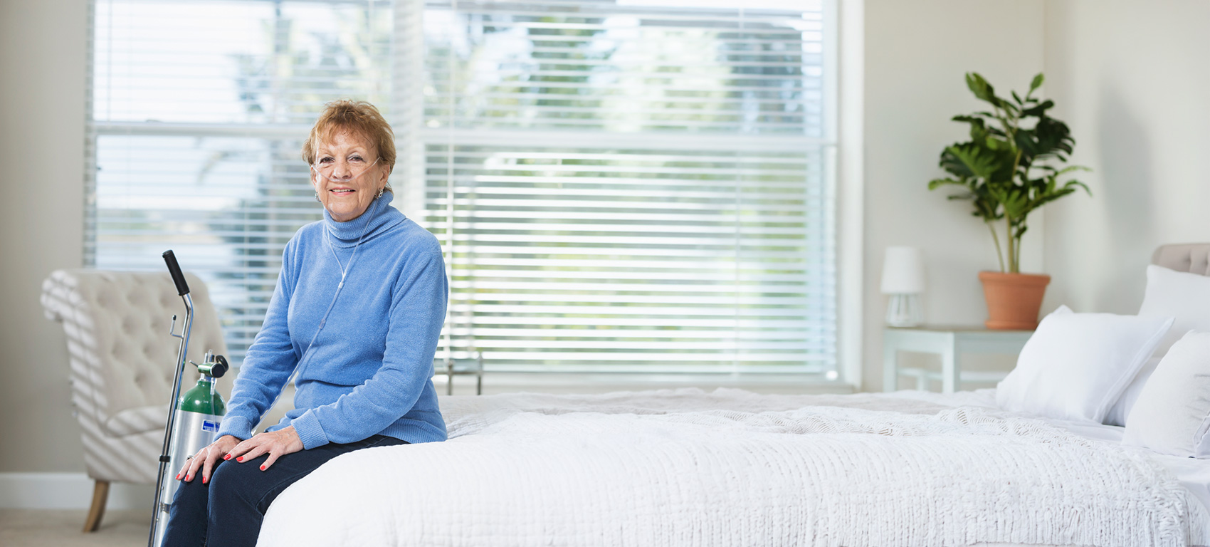Mujer mayor que utiliza oxígeno suplementario mientras está sentada en una cama
