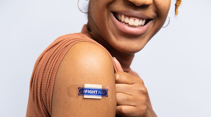 Mujer sonriendo mostrando su brazo donde tiene una curita que dice “Combate la gripe” en inglés.
