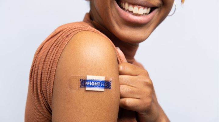 Mujer sonriendo mostrando su brazo donde tiene una curita que dice “Combate la gripe” en inglés.
