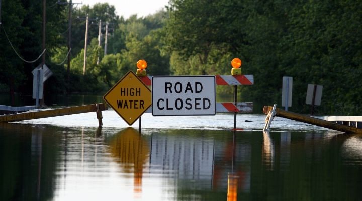 Calle inundada con señales en inglés de agua alta y carretera cerrada.