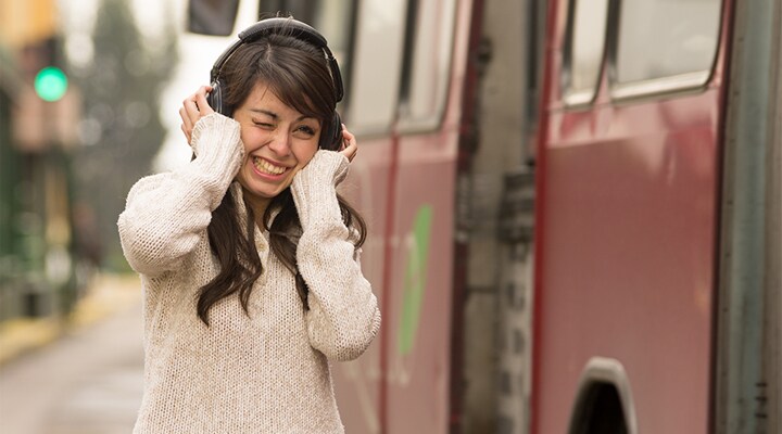 Una mujer afuera con unos audífonos apretando sus oídos.