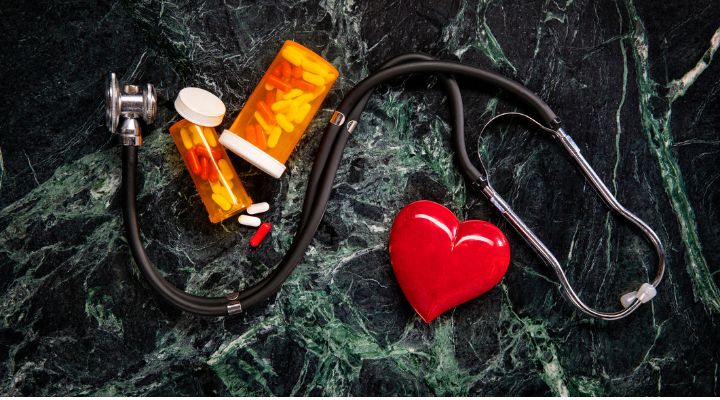 Un estetoscopio, botellas de medicina, y un corazón rojo sobre un fondo oscuro