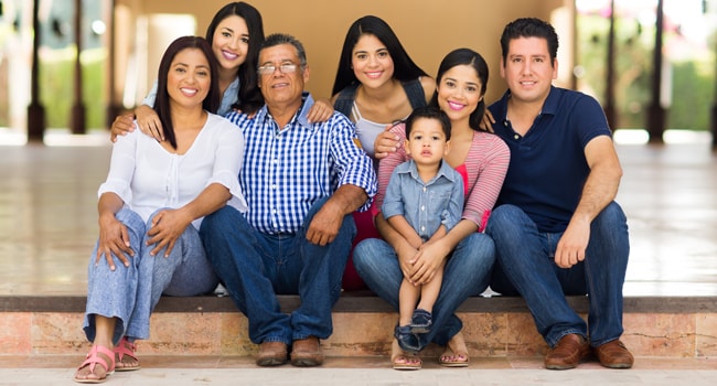 Familia latina, padres, hijos, abuelos y nietos sentados sonriendo.