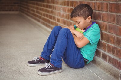 Un niño triste que está sentado contra una pared.