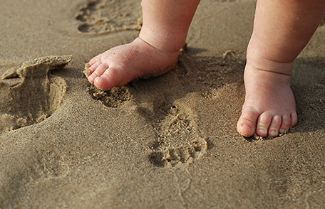 Pequeños pies de bebé dejando pequeñas huellas en la playa.