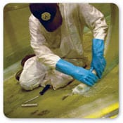 Vista delantera de un trabajador arrodillado usando guantes de caucho al aplicar barniz en el suelo