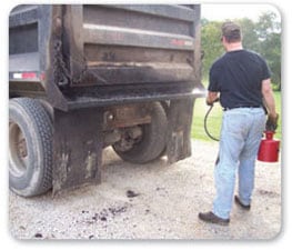 Vista posterior de un trabajador parado detrás de un camión usando guantes protectores mientras aplica productos de asfaltado