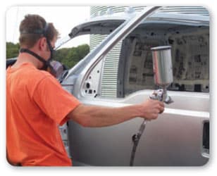 Vista lateral de un trabajador de la cintura hacia arriba usando protección respiratoria mientras aplica barniz en el costado de un camión