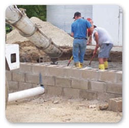 Vista posterior de dos trabajadores parados mientras aplican concreto usando calzado protector pero sin guantes