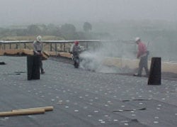 Figura 1. Trabajadores que aplican asfalto caliente al fieltro de fibra de vidrio (en el techo).