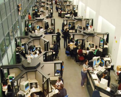Centro de despacho de llamadas 911 del Departamento de Policía de Nueva York que cuenta con un diseño en un área abierta en el cual las personas laboran muy cerca de las otras. 