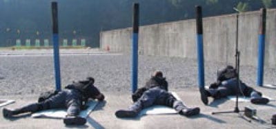 Vista posterior de 3 agentes del orden público boca abajo mientras participaban en una práctica de tiro en un campo al aire libre.