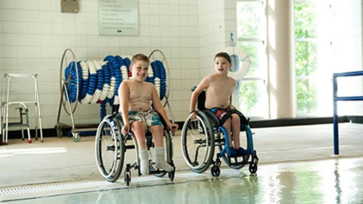 Kids with spina bifida smiling near an indoor pool