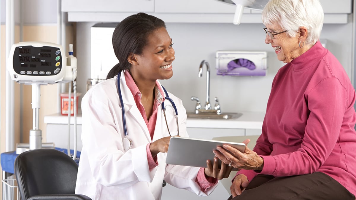 Doctor talking with elderly patient and showing her something on a tablet