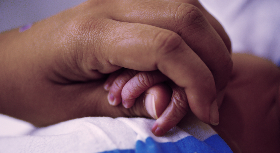 adult hand holds infant hand