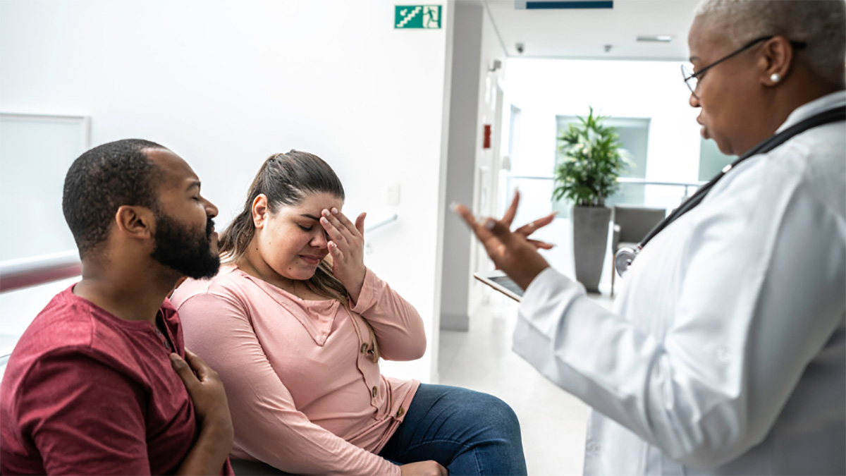 M&eacute;dico con portapapeles hablando con una pareja joven.