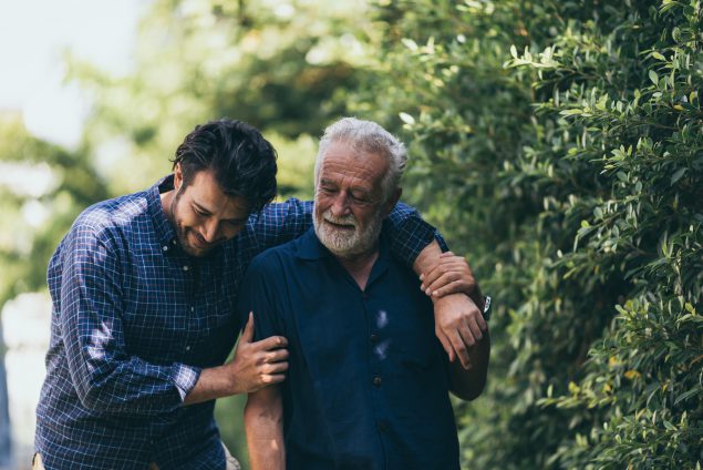 The old man and his son are walking in the park. A man hugs…
