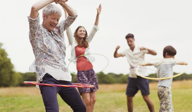 Playful multi-generation family spinning in plastic hoops in field
