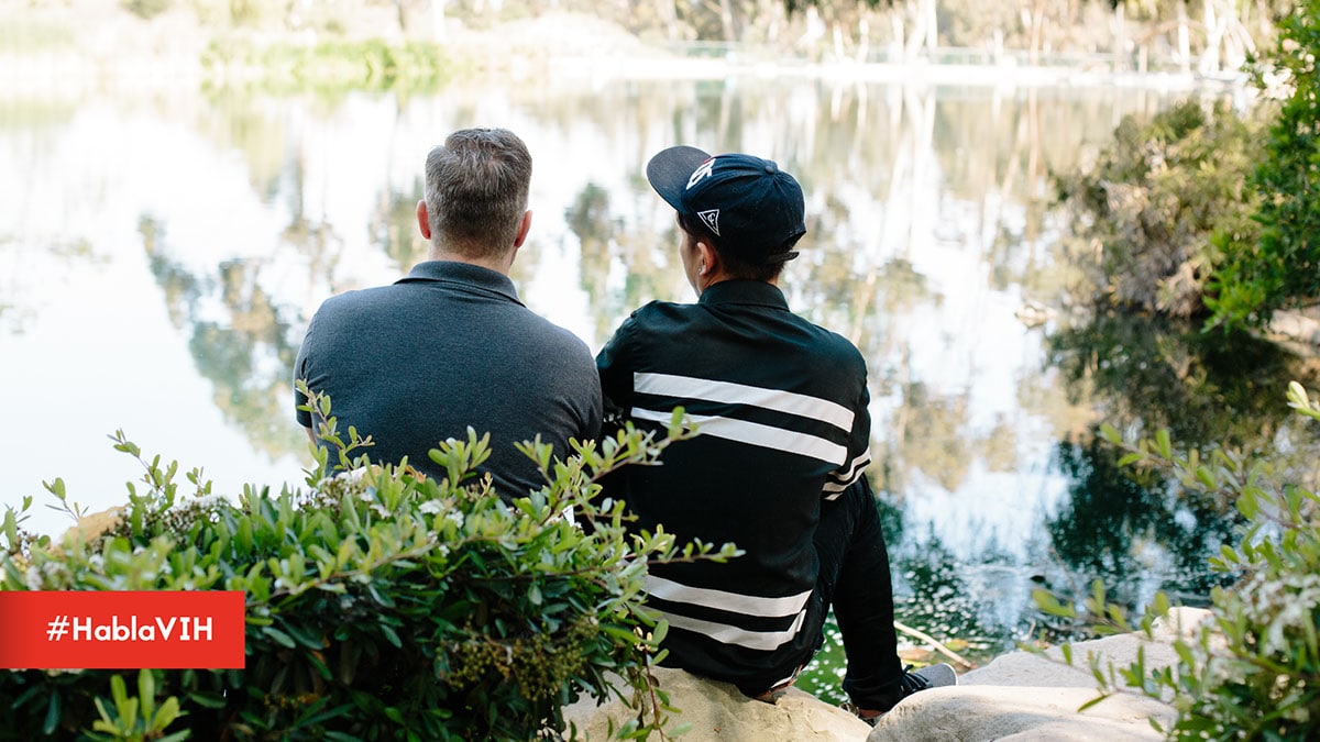 Two men sitting together outside facing a lake. #HablaVIH