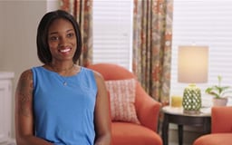 Black Female sitting in room with window and chair behind her talking to camera