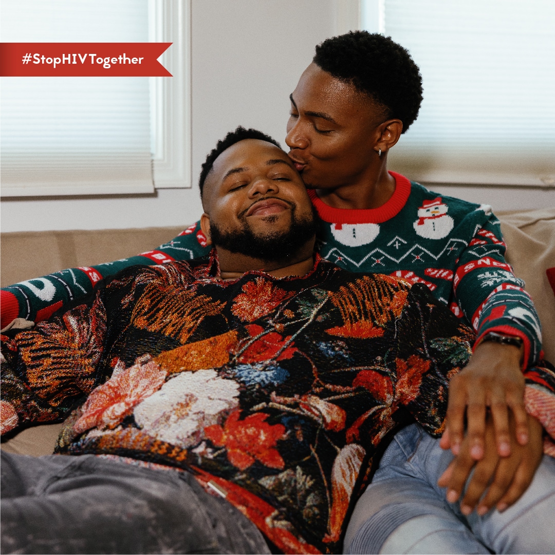 Dos hombres con suéteres festivos sentados en un sofá, disfrutando juntos de la temporada con el hashtag stophivtogether.