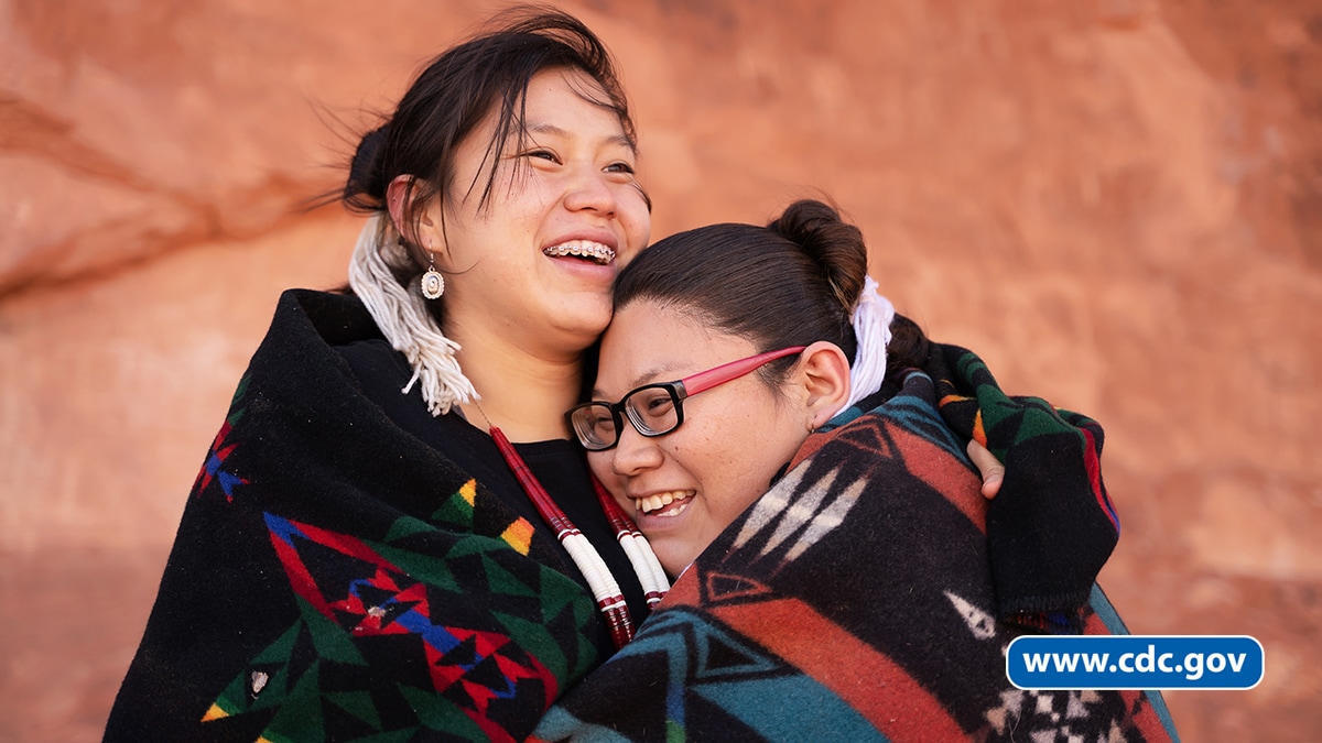 Two Native American/Alaska Native women hugging and smiling.