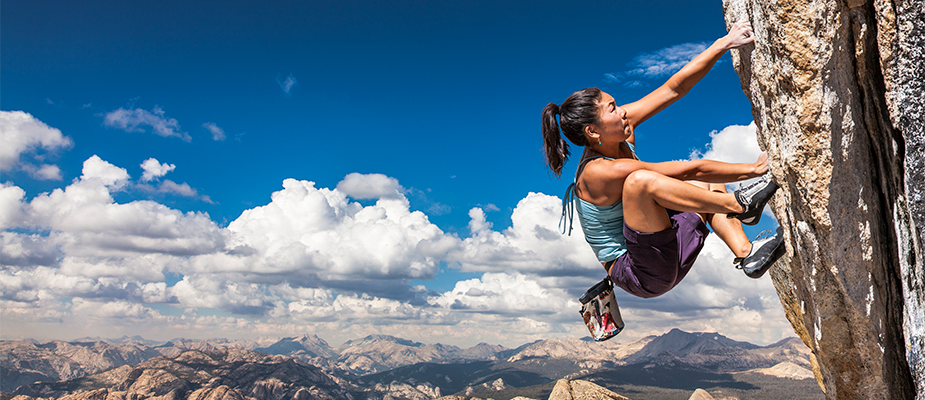 woman climbing an outdoor rock wall with sky and mountains in the background