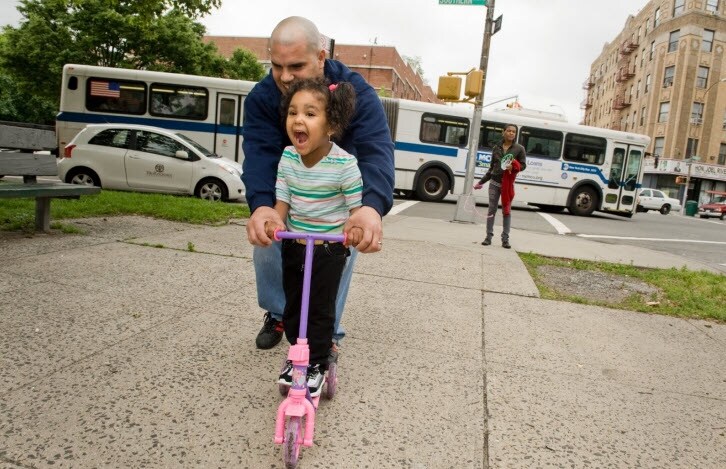 father teaching little girl to ride a scooter