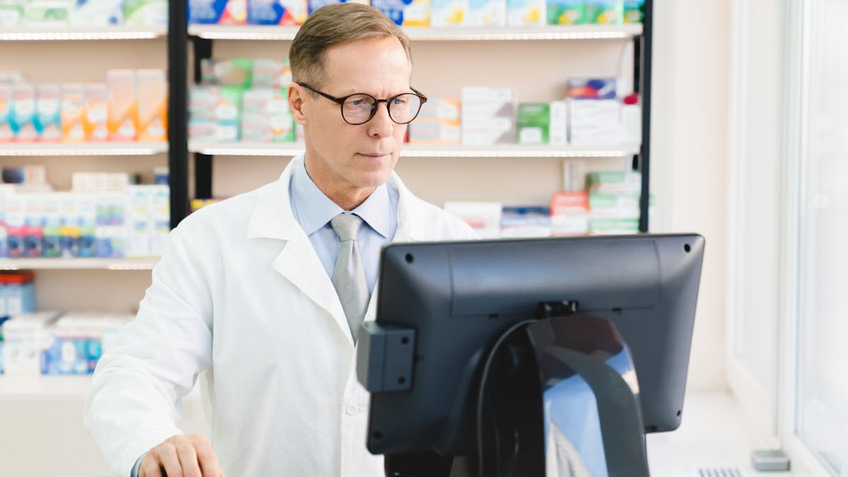 A male pharmacist reviews information on a pharmacy computer