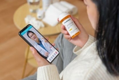 Woman reading prescription bottle while video chatting with doctor