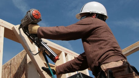 A construction worker uses a nail gun to build a house.