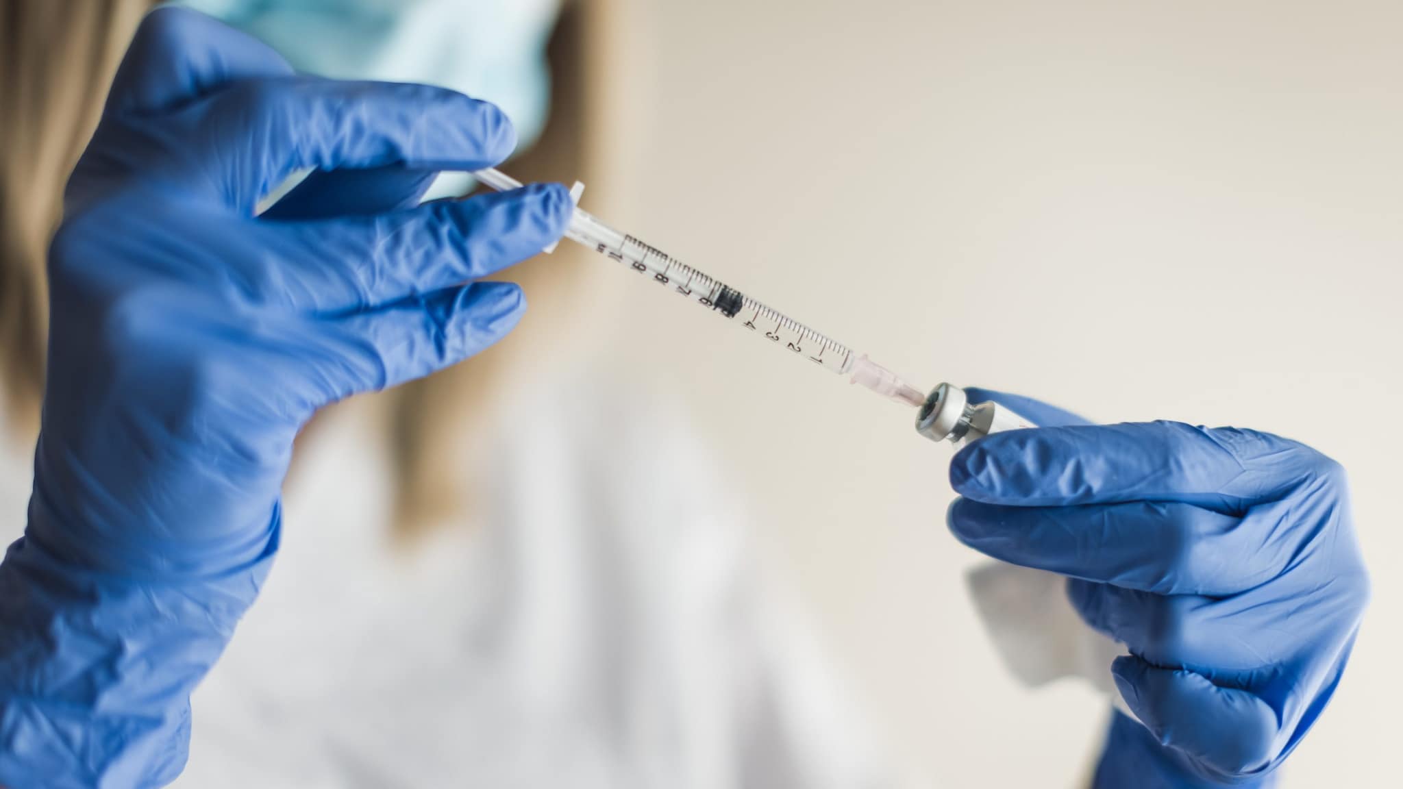 Healthcare professional inserting a syringe into a vaccine vial