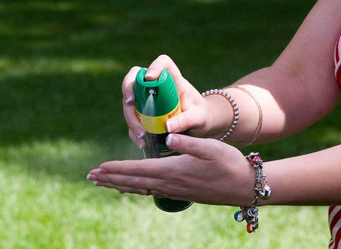 Photo of a woman spraying repellent into her hand to then apply to her face.