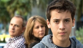 Adolescent male teen with parents in background