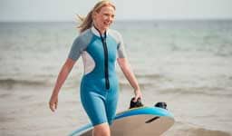 Mujer caminando por la playa con una tabla para surfear 