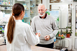 Hombre sonriente recibiendo medicación de su farmacéutico.
