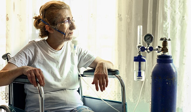 Woman in wheelchair receiving oxygen from a tank.