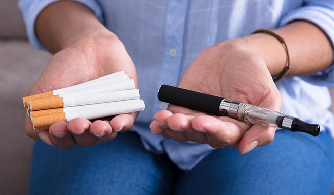 Woman holding cigarettes in one hand and an e-cigarette in the other hand.