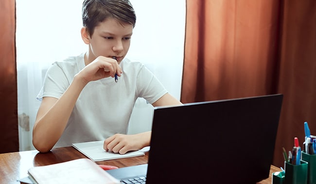 Estudiante mirando la computadora, viendo clases de educación en línea o seminarios web en casa.