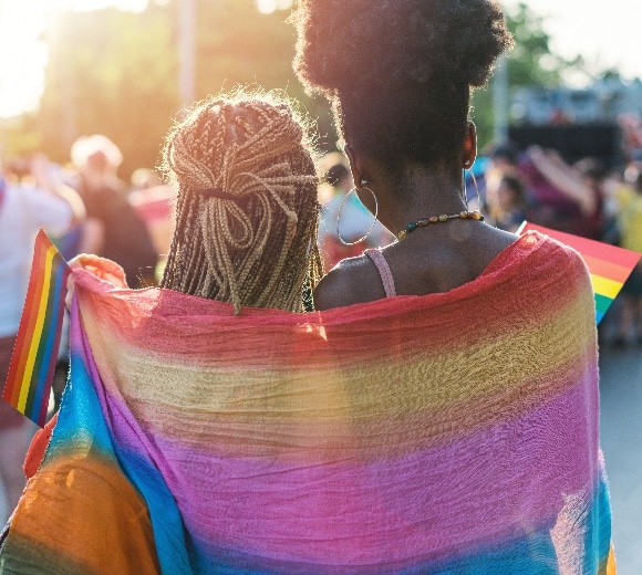 Young female couple hugging with rainbow scarf at a pride event