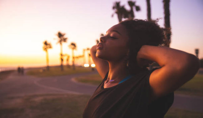 woman with her arms over her head taking a deep breath outside