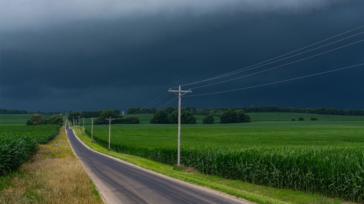 Isolated road along a grassy field with a dark, stormy sky
