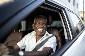 Smiling senior man driving a car and looking at camera