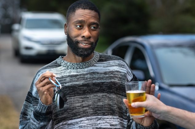 A guy holding car keys while being offered an alcoholic drink