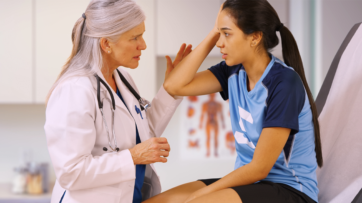 Doctor talks with young patient gesturing towards her head