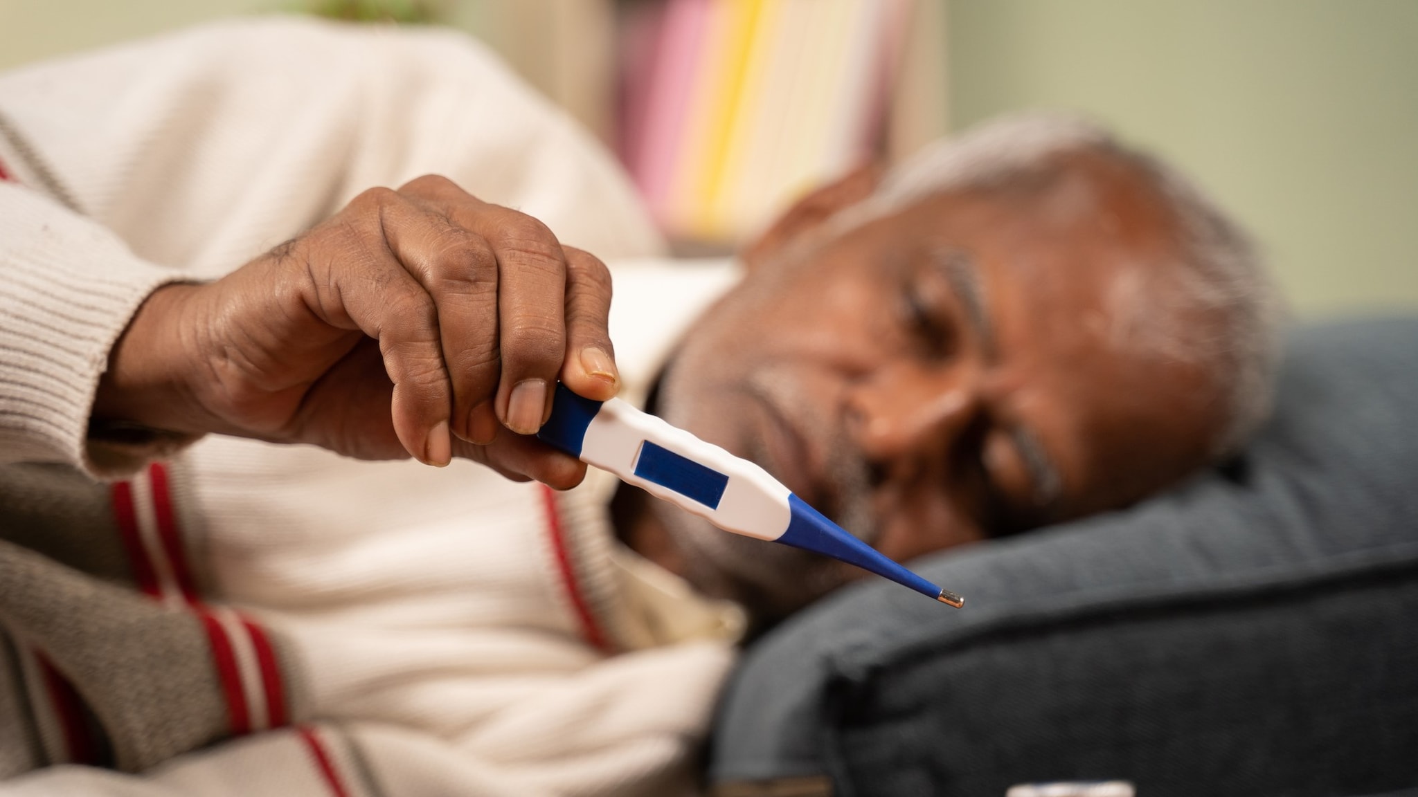 An older adult lying on their side holding a thermometer in their hand.