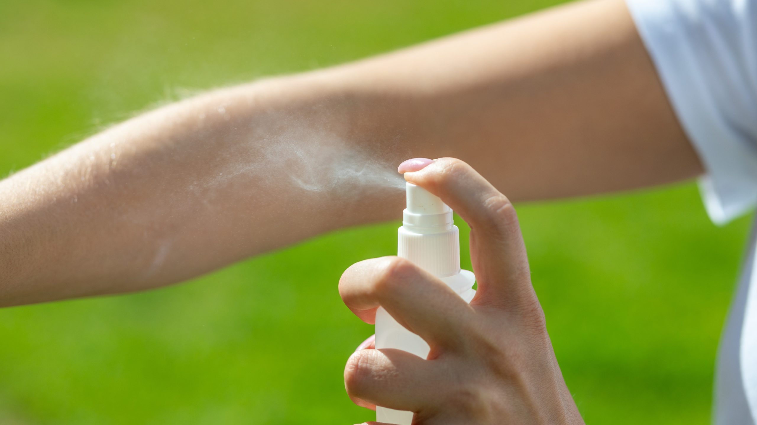 A person spraying insect repellent on their arm.