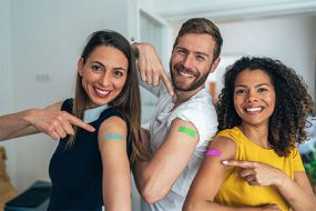 Tres adultos se&ntilde;alando las curitas en la parte superior de sus brazos.