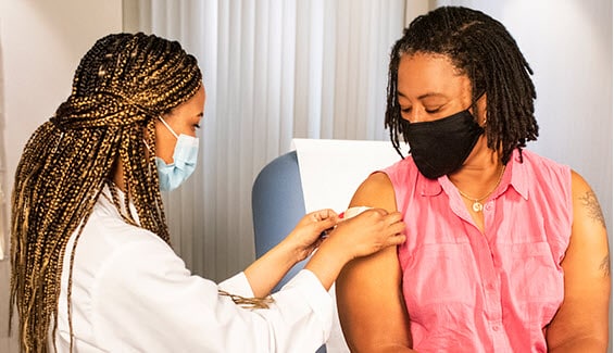 Doctor wearing face mask puts bandaid on woman's arm after immunization
