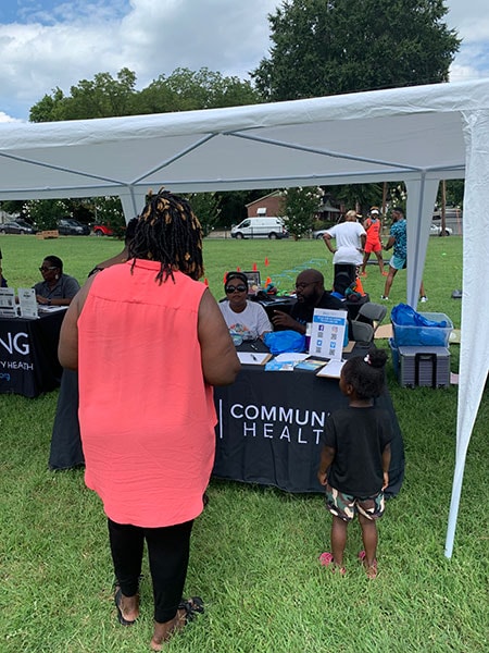 Mother and child stand in front of a outdoor community health booth